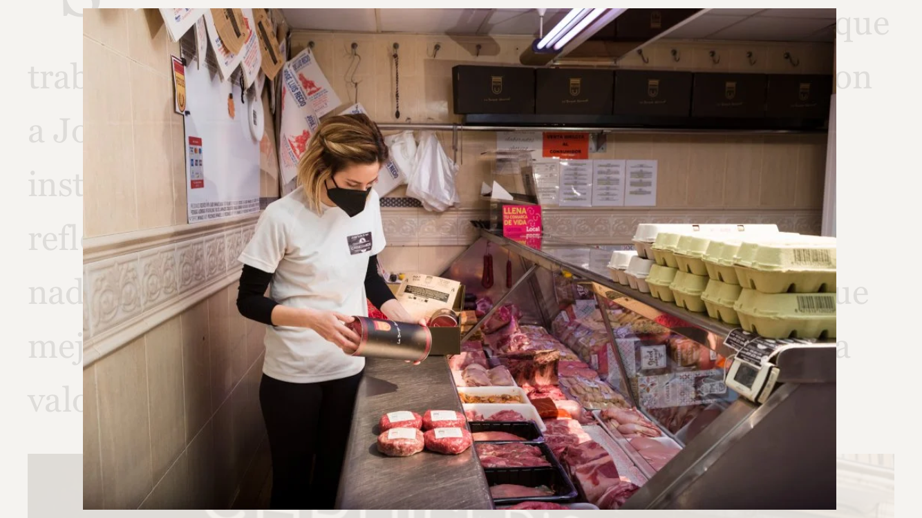 Una imagen que muestra a un carnicero atendiendo a un cliente detrás del mostrador, mostrando diferentes cortes de carne en una carnicería elegantemente decorada.